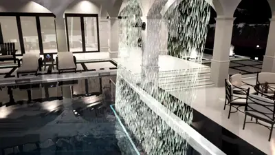 Rain curtain water wall beside a dining terrace, house windows lit behind