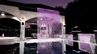Magenta-lit rain curtain at night with the pool mirroring the arches